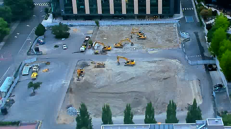 The overall scene remains quite similar, though a small, dark-colored vehicle has entered the site via the driveway on the left.
