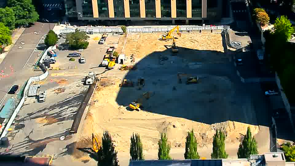 A white pickup truck has entered the site via the driveway on the left side of the frame and is now parked near the equipment. Otherwise, the scene appears static, with the machines and material distribution holding their previous positions.
