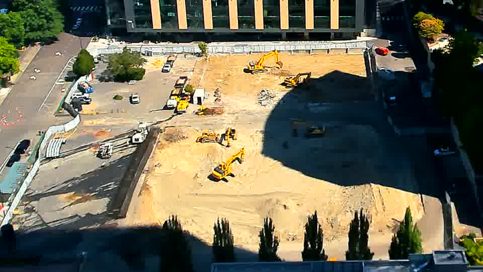 The white pickup truck that arrived earlier has now moved further into the site, closer to the center of the work area. Otherwise, the machines and material stockpiles maintain their previous arrangement.