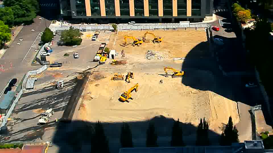 A small white vehicle has pulled onto the site from the driveway on the left, parking near the other equipment, and a slight rearrangement of material is visible near the center of the work area.
