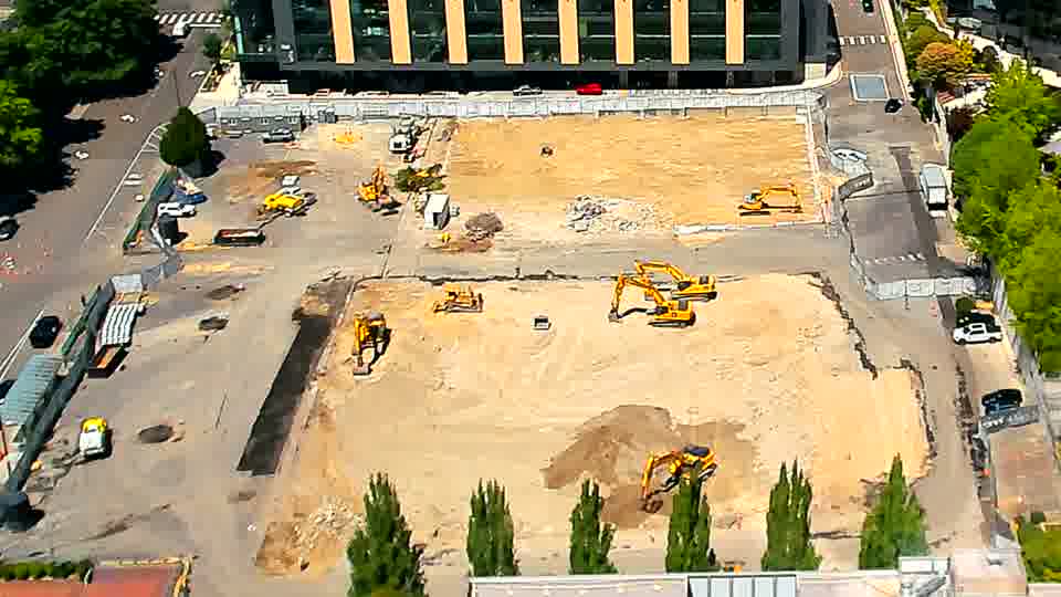 A white vehicle is now visible on the service road at the right edge of the frame, and one of the excavators near the center has subtly altered its orientation.