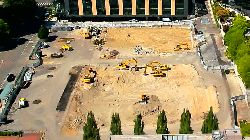 The equipment layout is largely unchanged, though a light-colored truck is now visible exiting the driveway on the left side of the frame.