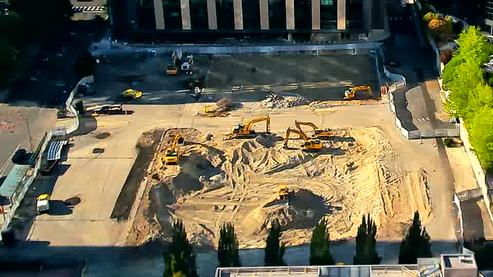 The equipment and stockpiles on site maintain their positions, though the sunlight now casts slightly different shadows.