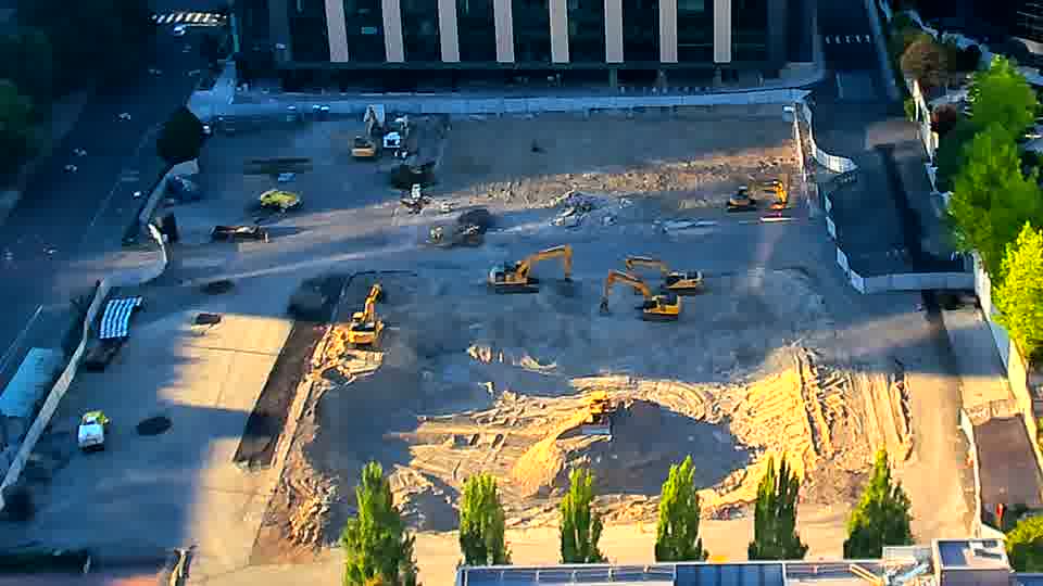 The shadows have shifted across the site, but the positions of the machines and material stockpiles remain largely unchanged.