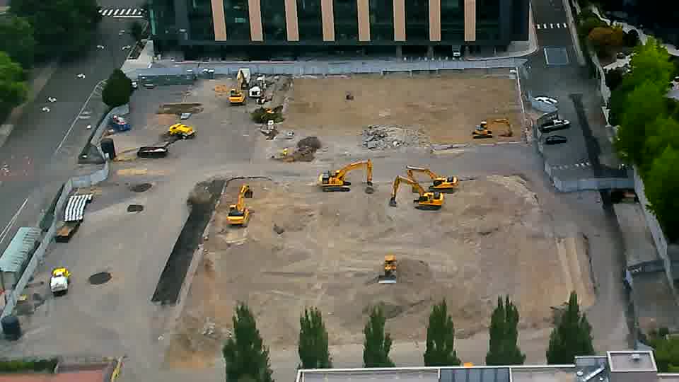 The arrangement of machinery across the site remains stable, though a yellow vehicle has appeared near the driveway on the left.