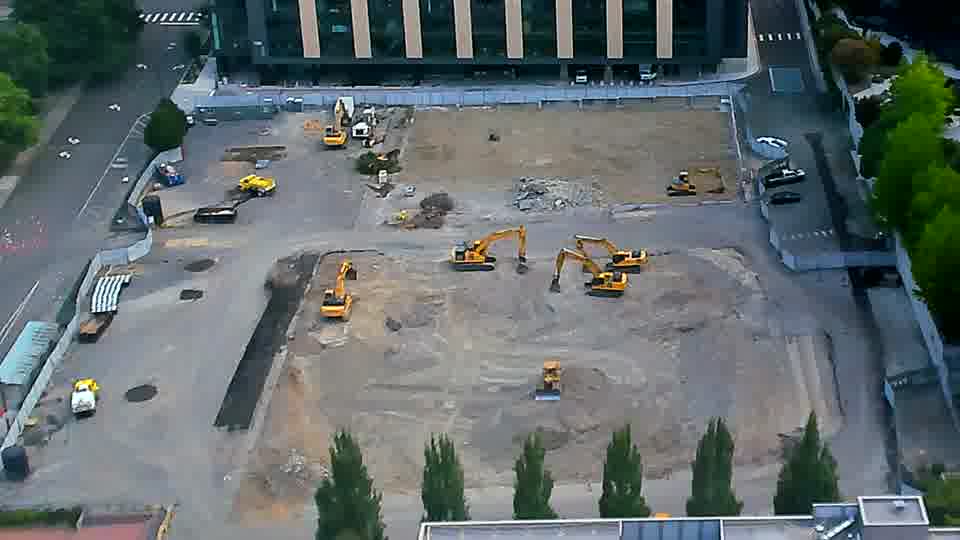A yellow machine has shifted slightly towards the center of the site from its position near the left-side driveway.