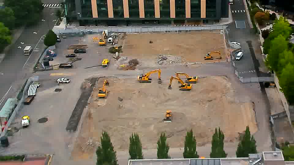 Equipment positions are static, though a white van has entered the site via the driveway on the left.