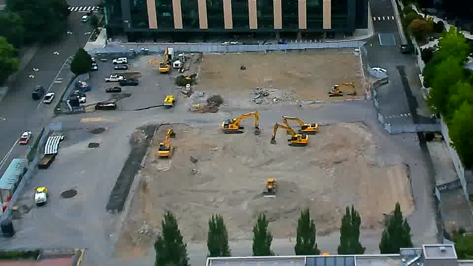 A small white vehicle has moved from near the left edge to a position further into the site. Otherwise, the equipment and overall scene appear unchanged in the last quarter hour.