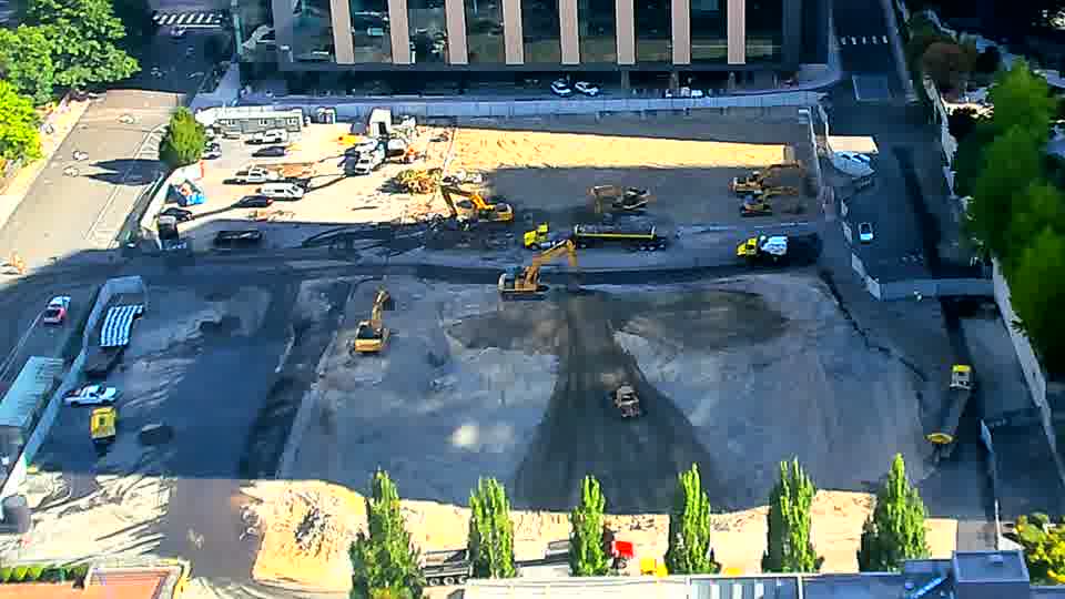 A small, white pickup truck has entered the site through the driveway on the left side of the frame and is now parked near the equipment.