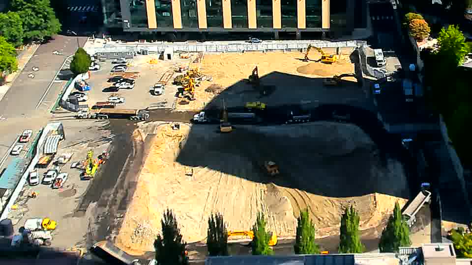 A white pickup truck has entered the site via the driveway on the left side of the frame. Otherwise, the arrangement of equipment and materials appears consistent between the two views.