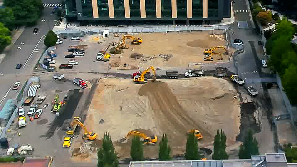 A number of vehicles have gathered near the service road on the right side of the frame, and one appears to be departing. Otherwise, the positions of the heavy equipment across the site remain largely unchanged.