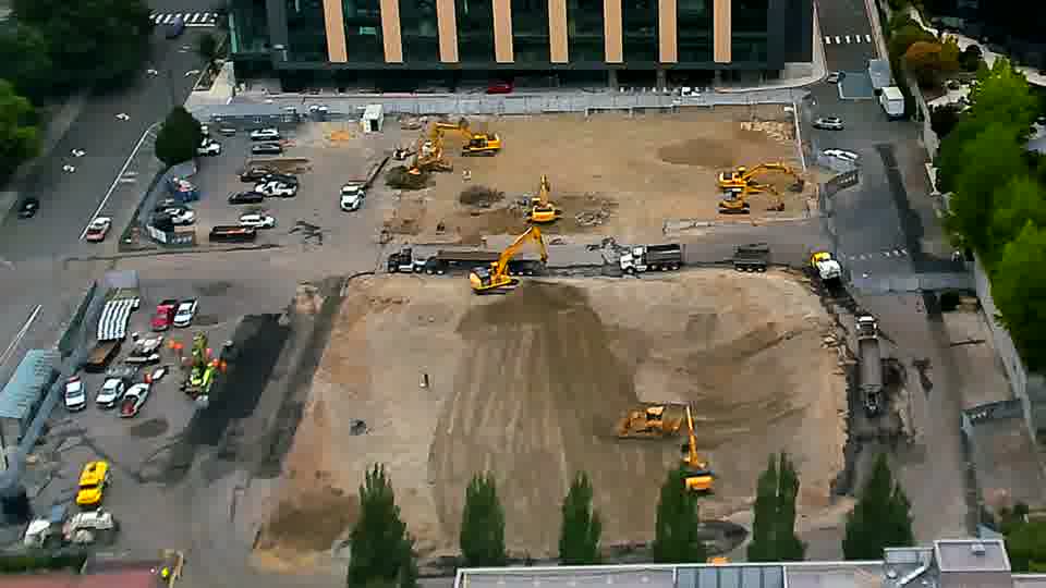 The machines on site seem to hold their places, though one excavator near the center has raised its arm.
