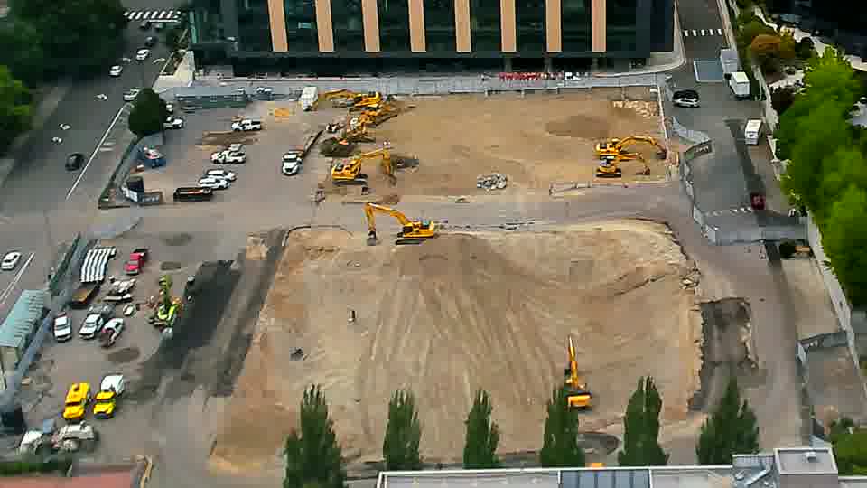 The arrangement of heavy equipment across the site holds steady, with no discernible movement of machines or vehicles in the last fifteen minutes.