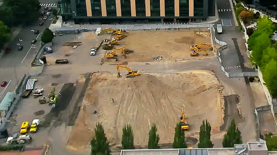 A white van has entered the site through the driveway on the left side of the frame. Otherwise, the arrangement of equipment and materials appears to be consistent with the prior view.