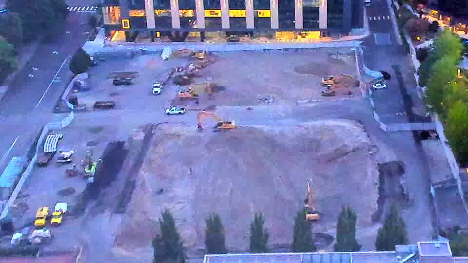 The site is now visible in daylight, revealing several pieces of heavy machinery across the graded area. Conditions appear stable with no apparent movement of equipment or vehicles between the frames.