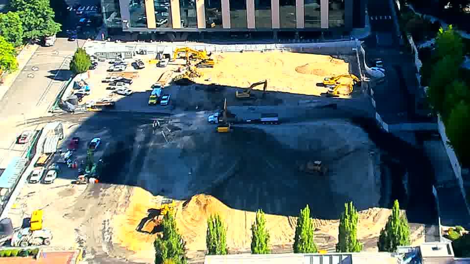 The central excavator that was facing slightly left has now turned further to the right, and a small blue vehicle is visible near the driveway on the left.
