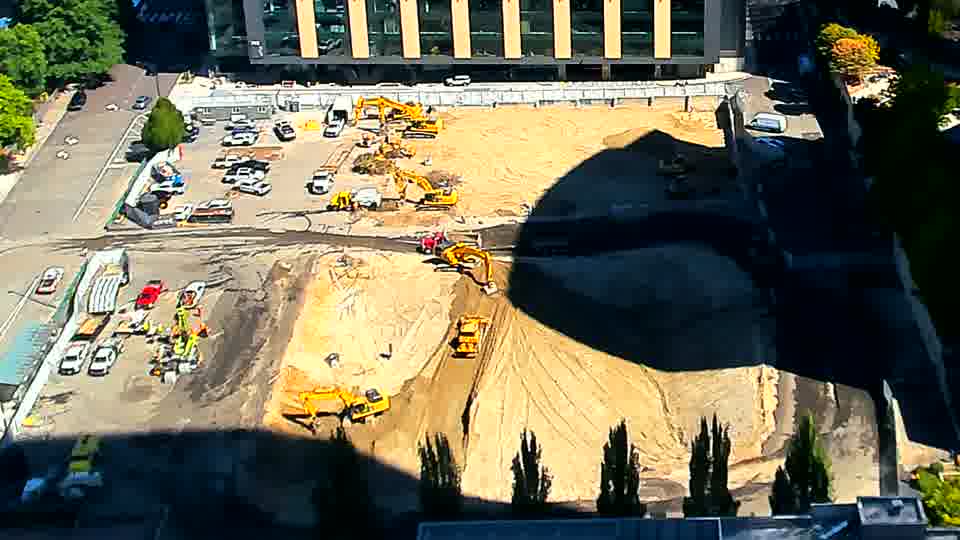 The excavator in the foreground is now angled more sharply towards the center of the site, and its arm is extended.