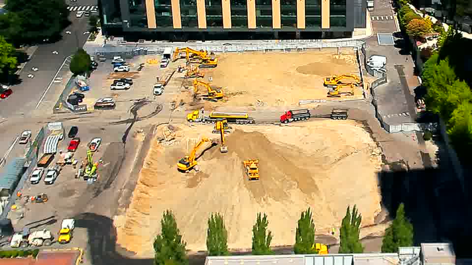 The arrangement of heavy equipment remains largely unchanged, though a small white vehicle has joined the line near the driveway on the left.
