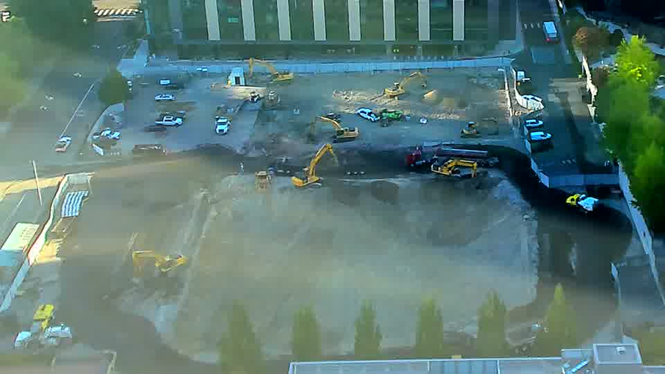 A yellow excavator near the center of the site has shifted its position slightly.
