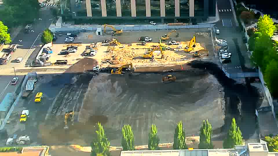The yellow excavator closest to the bottom of the frame has noticeably moved to the right.