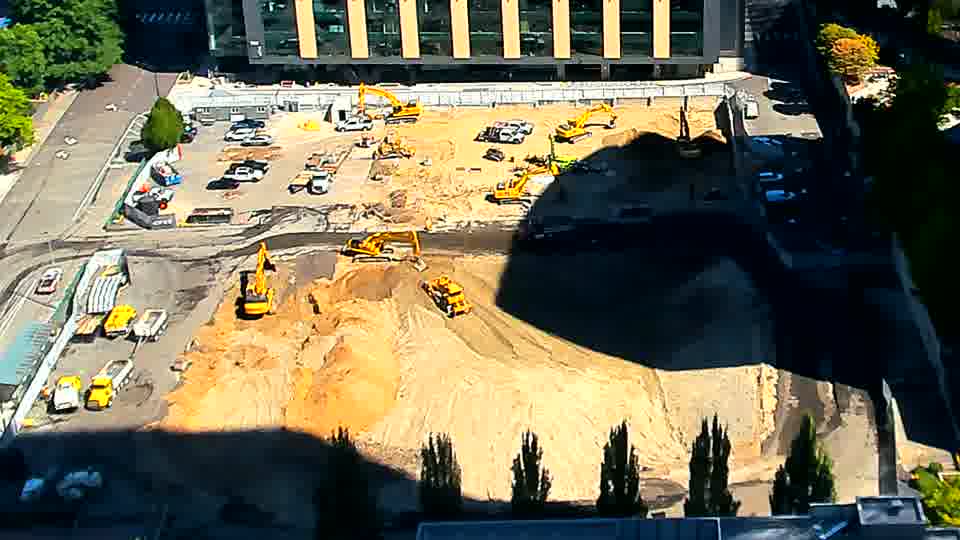 The position of one of the excavators near the center of the site has shifted slightly. Otherwise, the arrangement of equipment and materials remains largely unchanged between the two views.