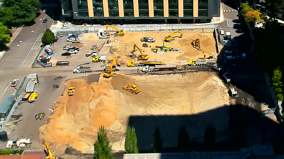A large dump truck is now exiting the site via the driveway on the left. Otherwise, the equipment and materials on site remain in largely the same positions.