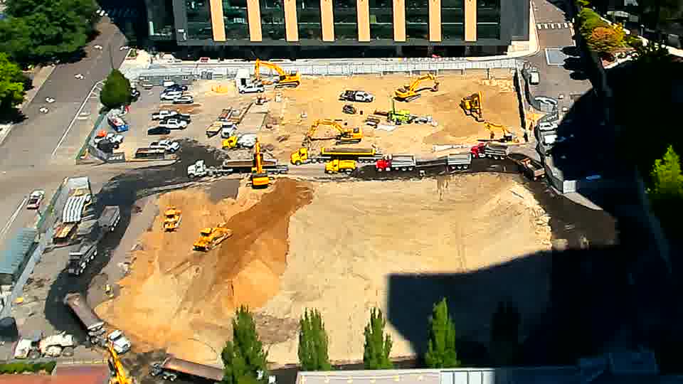 The position of an excavator near the lower-center of the site appears to have been adjusted slightly. Otherwise, the machines and materials across the block maintain their previous arrangement.