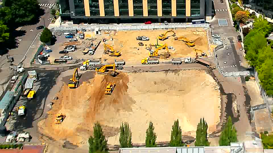 A white truck has repositioned along the central transit path, and one excavator near the center has adjusted its stance slightly — all other machinery and materials remain stationary.