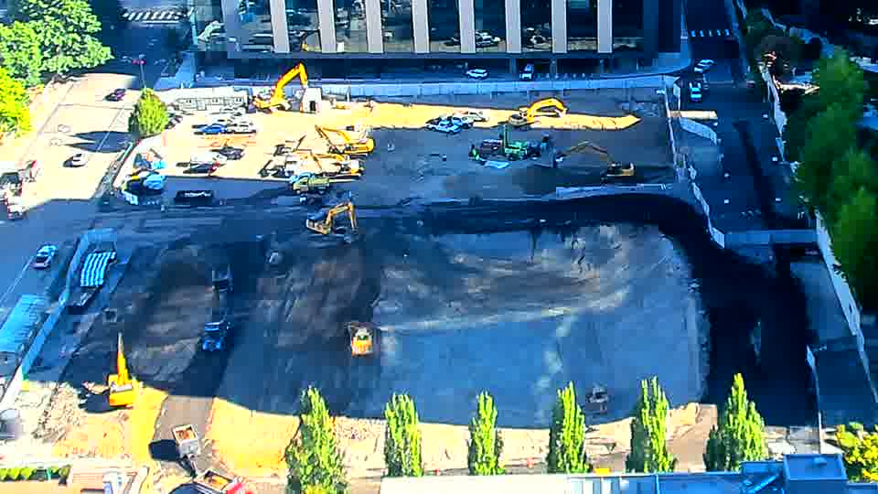 A small yellow machine has appeared near the lower-right corner of the site, and the arrangement of materials in the central area seems subtly different. Otherwise, the equipment and overall scene stay as they were.