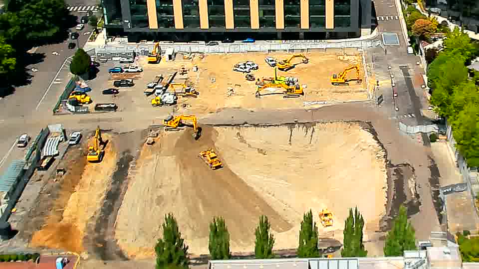 A smaller, yellow machine has moved from the lower-right to the center of the graded area. The rest of the site's equipment and materials remain in similar positions.