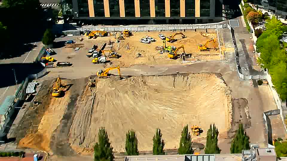 The machinery across the site remains in roughly the same arrangement as before, although a darker patch of earth is now visible in the lower-right corner.