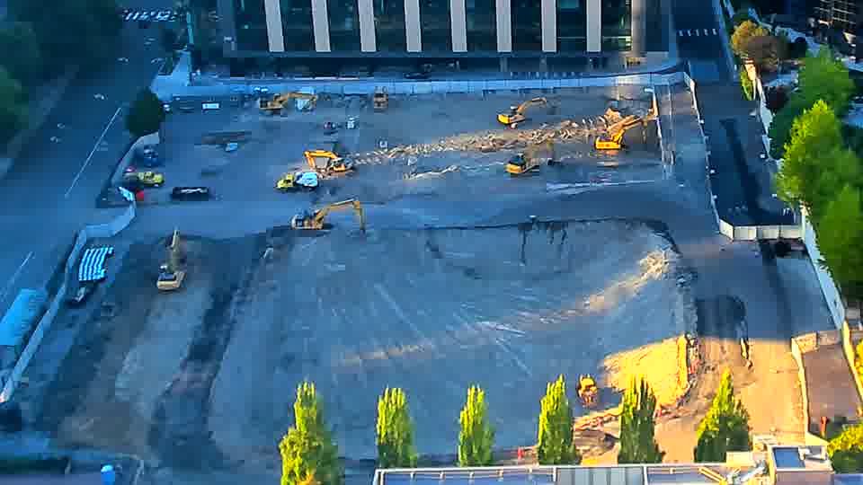 A small, yellow machine has appeared near the service road on the right side of the frame. Otherwise, the site maintains a similar appearance to the previous view.