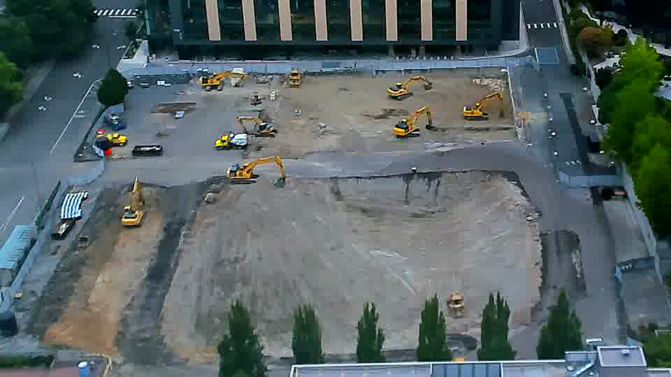 The arrangement of equipment appears nearly unchanged, though a dark-colored vehicle has entered the site via the driveway on the left.