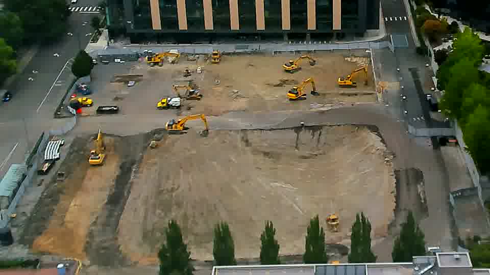A small white vehicle has moved from the staging area near the driveway on the left to a position closer to the center of the site.