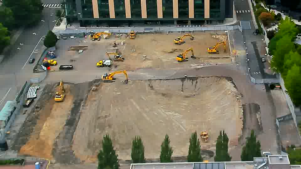 The equipment across the site appears to be in the same positions as before, though a dark-colored truck is now visible entering the driveway on the left.
