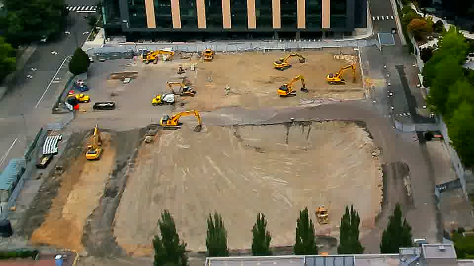 A small group of people are now visible near the center of the site, appearing to be observing the graded area. Otherwise, the layout of equipment across the site remains consistent with the previous view.