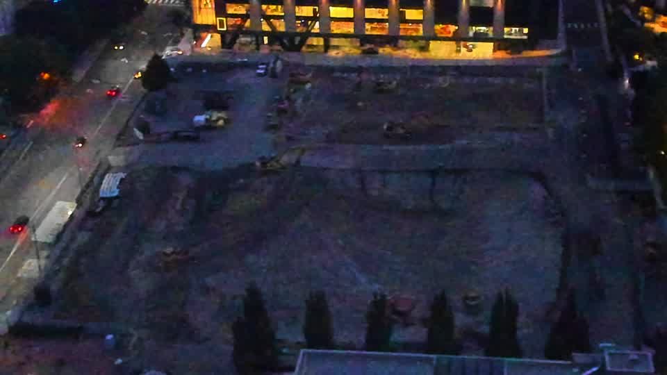 The site appears largely unchanged, though some additional shapes are now visible within the center of the graded area. Visibility remains low, with city lights reflecting off the surface.