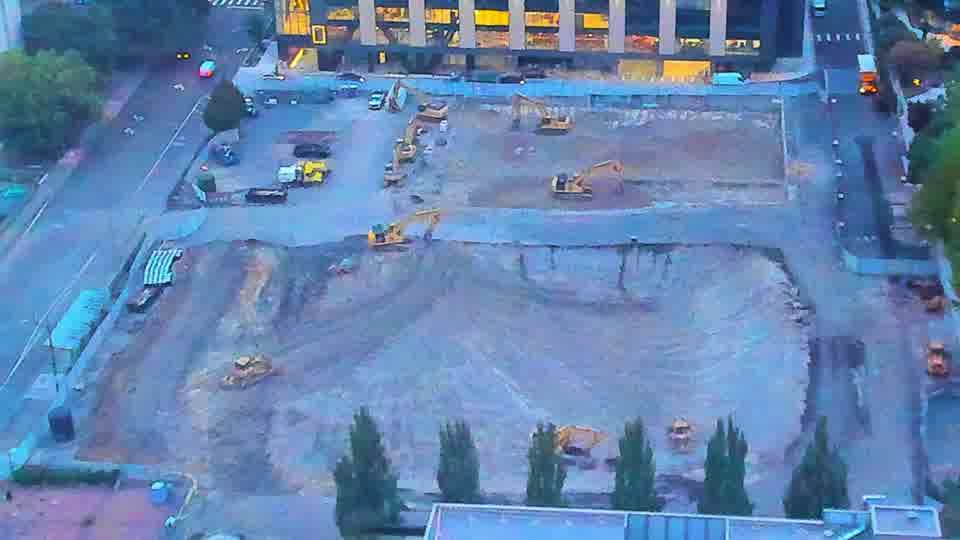 The scene is brighter now, revealing several pieces of heavy equipment positioned across the graded area. Otherwise, the layout of the site remains consistent between the two views.