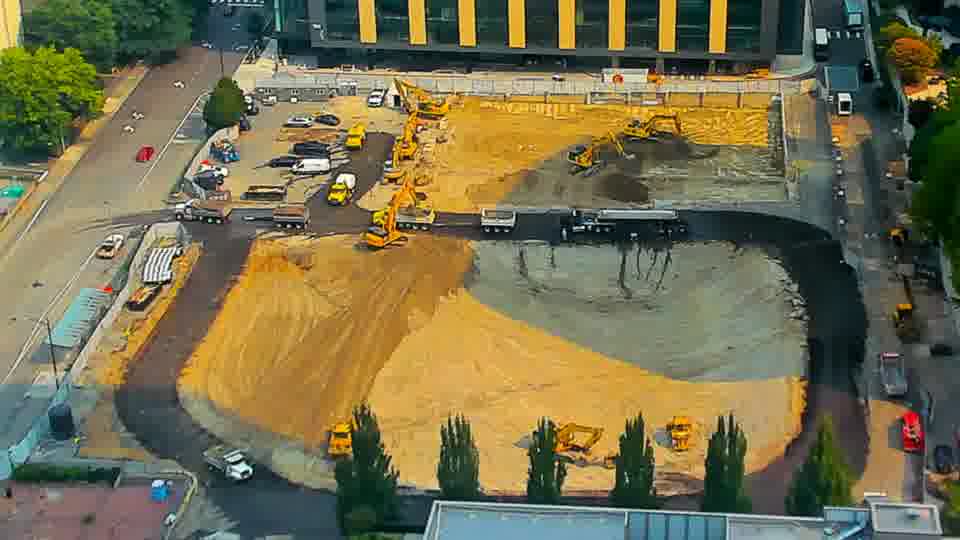 The arrangement of equipment across the site is largely static, though a light-colored truck has entered the driveway on the left side of the frame.