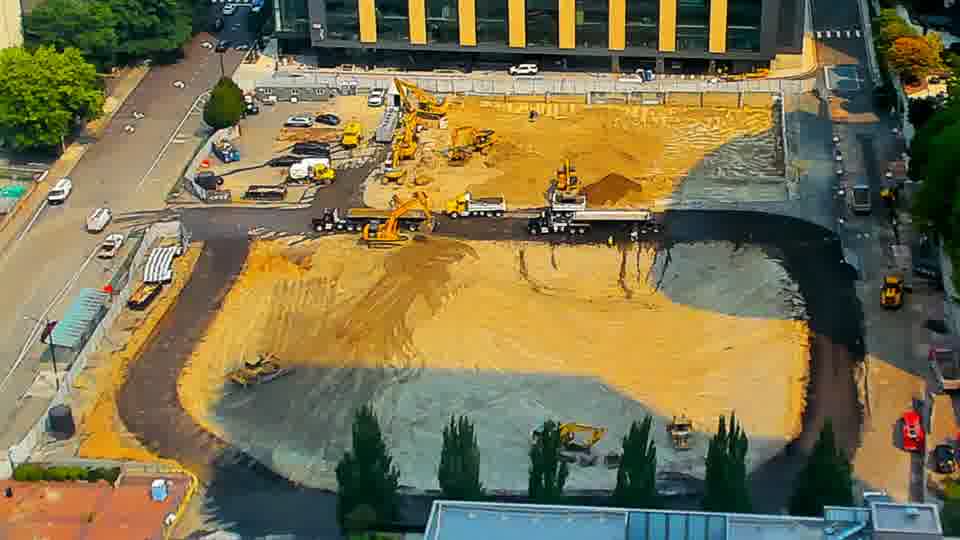 A small, dark-colored vehicle has moved from the service road on the right to a position near the center of the site.