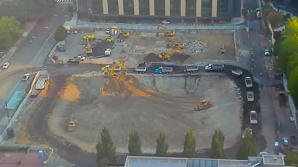 A dark-colored truck has entered the site via the driveway on the left side of the frame, and is now positioned along the central area. Otherwise, the overall scene remains largely unchanged, with the equipment holding its positions.