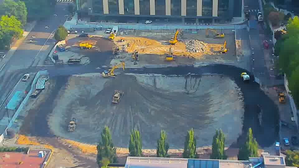 The tracked dozer near the center has shifted slightly to the right, and a small white vehicle is now visible moving along the worked area.