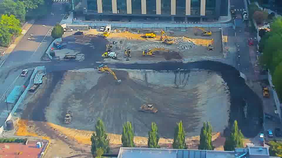 The excavator near the center of the frame is now positioned further to the south, actively working in the graded area.