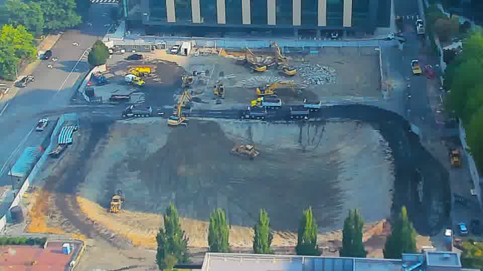 A small dark-colored vehicle has moved further into the worked area from the left side of the frame.