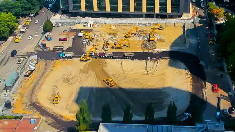A small yellow machine has moved from the upper-center to the lower-center of the worked area. Otherwise, the scene remains much as it was, with the same distribution of equipment and materials.