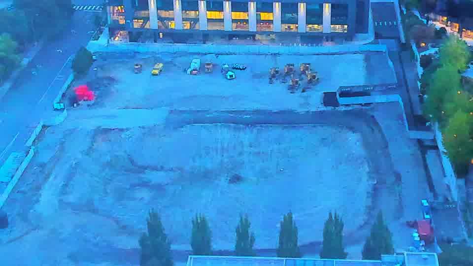 Construction camera frame at 6:30 AM PT. The site is now visible in daylight, revealing several pieces of machinery positioned across the graded area. The scene remains largely unchanged from 15 minutes ago, with the same equipment visible in the same locations.