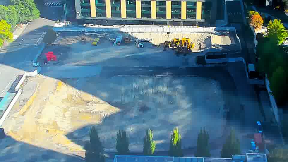 Construction camera frame at 9:45 AM PT. A blue truck has entered the site via the driveway on the left side of the frame. Otherwise, the equipment and materials within the block appear to be in the same locations.