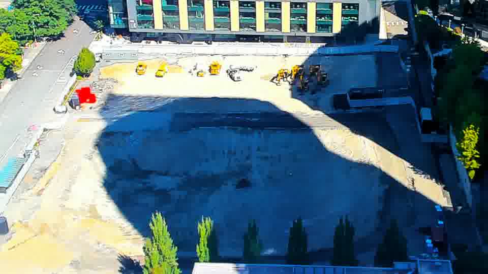 Construction camera frame at 11:30 AM PT. A yellow machine has shifted position slightly within the central area of the site. Otherwise, the equipment and materials appear to remain in place, and shadows continue to lengthen.