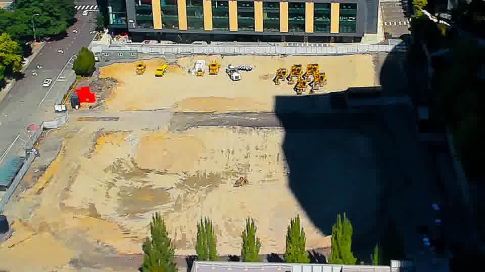 Construction camera frame at 12:15 PM PT. The scene presents a consistent view, with no observable movement of equipment or vehicles during this interval.