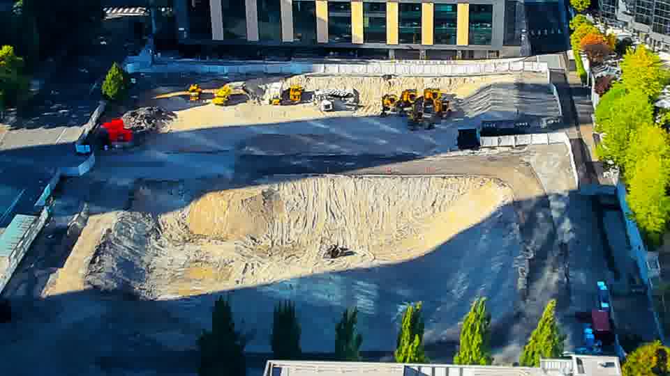 Construction camera frame at 5:00 PM PT. The red vehicle previously visible near the left edge of the frame is no longer present. Otherwise, the machinery and materials maintain their positions across the site.